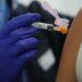 Nurse Wearing Purple Gloves Prepares a Syringe to Inject a Person's Upper Arm. - Regios Al Cuadrado