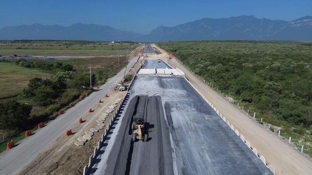 Carretera-interserrana 2 - Regios Al Cuadrado Aerial View of a Long Road Under Construction with Heavy Machinery Laying Asphalt, Barriers Along the Sides, and Green Fields with Distant Mountains. Peaceful Rural Landscape in the Background. - Regios Al Cuadrado