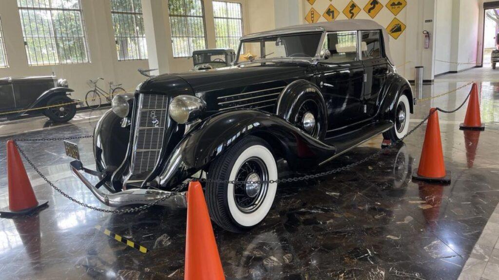 Museo-del-auto-monterrey-pádel - Regios Al Cuadrado Black Vintage Luxury Car on Display Indoors, Surrounded by Orange Cones and a Chain Barrier in a Showroom. - Regios Al Cuadrado
